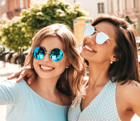 Two women with sun glasses on looking at a cell phone and taking a selfie